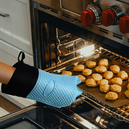 Blue five-finger silicone oven glove lifting a tray of biscuits from the oven